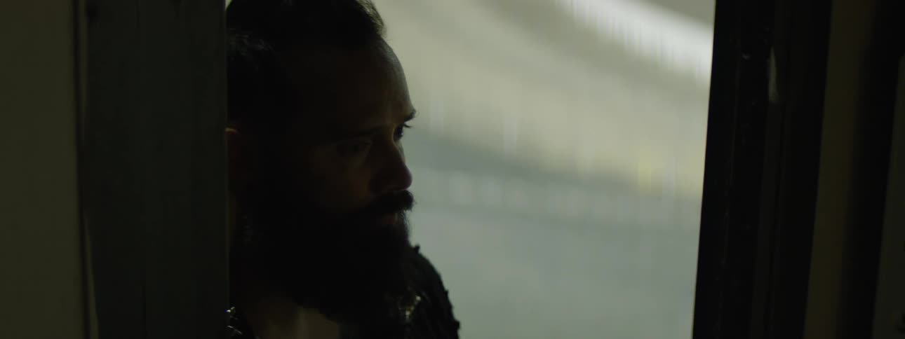 Bearded man looks thoughtfully through the doorway under soft light