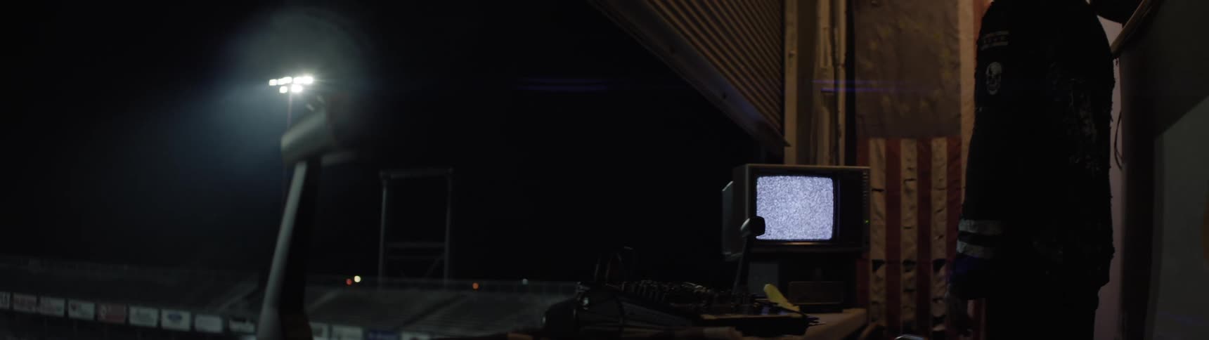 Old television displays static on a workbench surrounded by equipment under night lighting