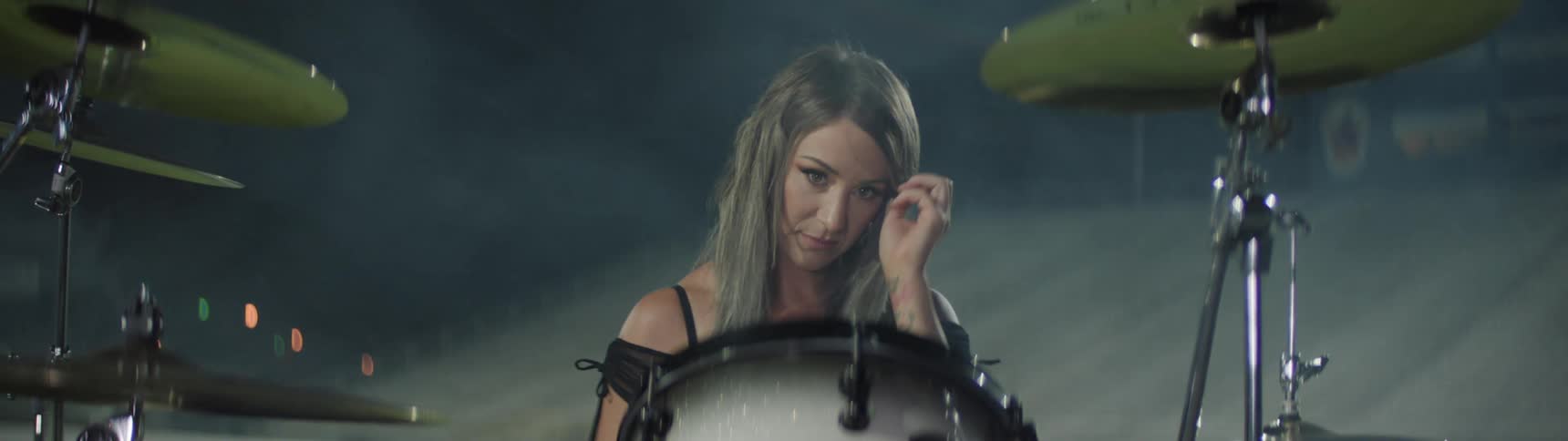 The drummer sits behind the drums and adjusts the cymbal