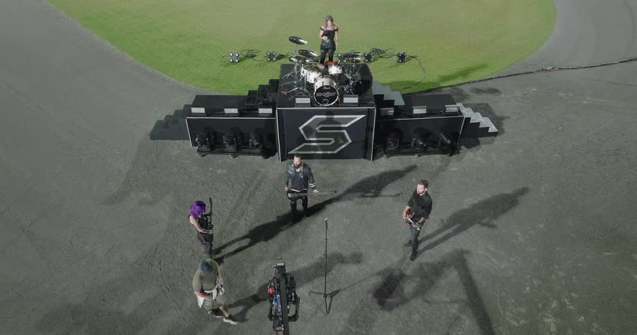 A musical band gathers on a field at night the area illuminated by lights as they prepare to practice