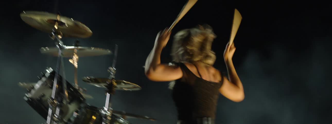 Woman playing drums intensely in a dark smoky setting