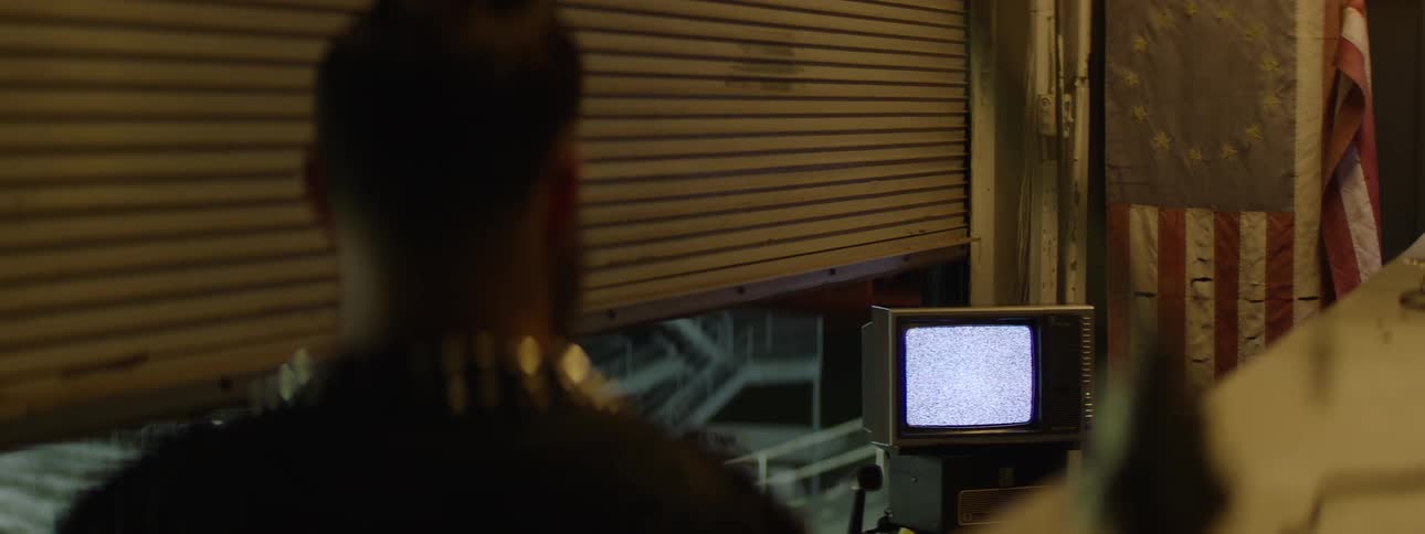 Person watching a staticfilled television in a dimly lit industrial setting