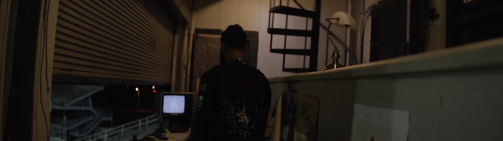 Person watches static monitor in dark room overlooking lit stadium