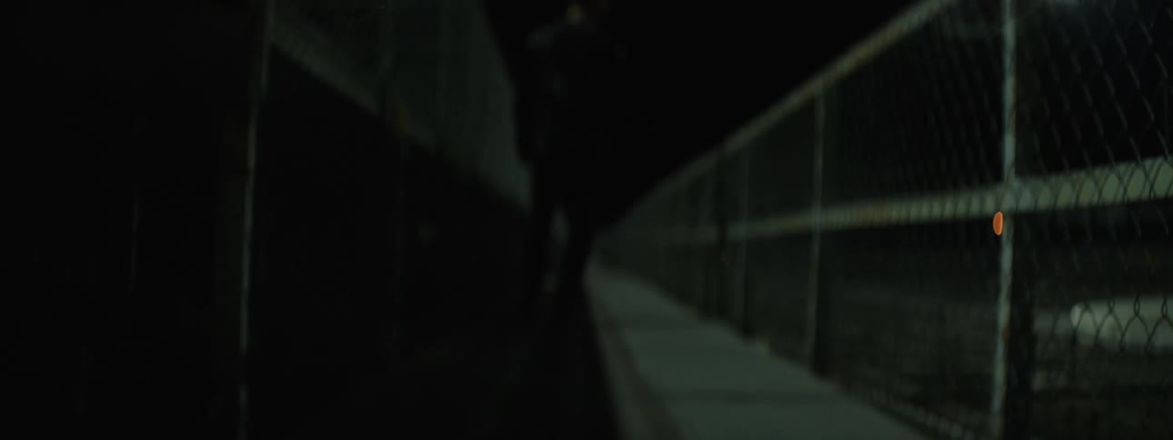 The video is a firstperson pointofview shot of someone running quickly through a dark narrow outdoor hallway or passageway the ground is made of dark wood and metal grates and the low light and motion blur create a sense of intense urgent mov