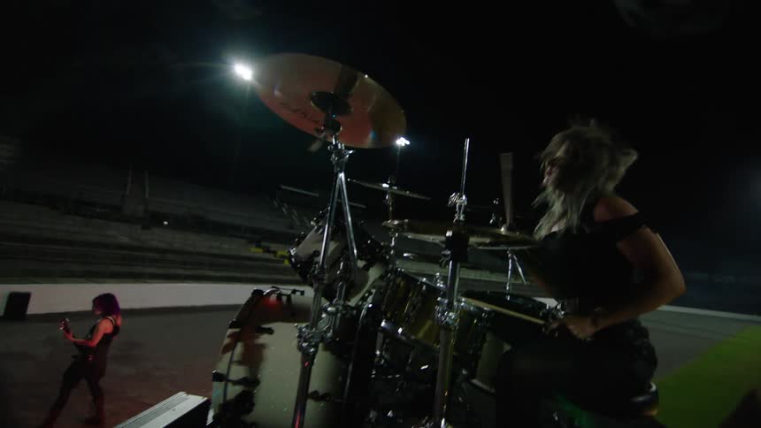 Drummer plays energetically on an outdoor stage lit up at night