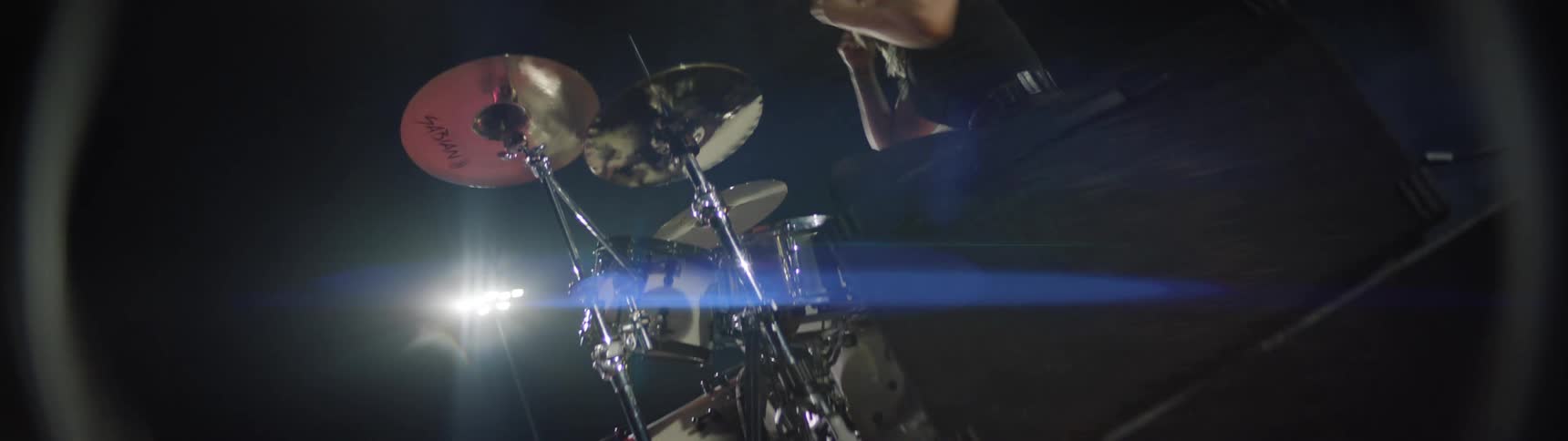 Drummer playing energetically under bright lights on a night stage