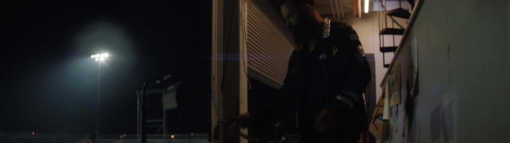 Man in a dark jacket walks through an industrial setting lit by artificial lights at night
