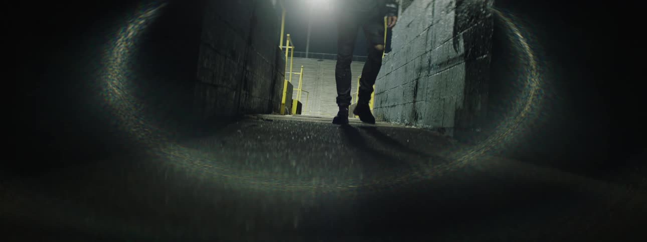 Person walking through a dark corridor lit by a bright light in the background