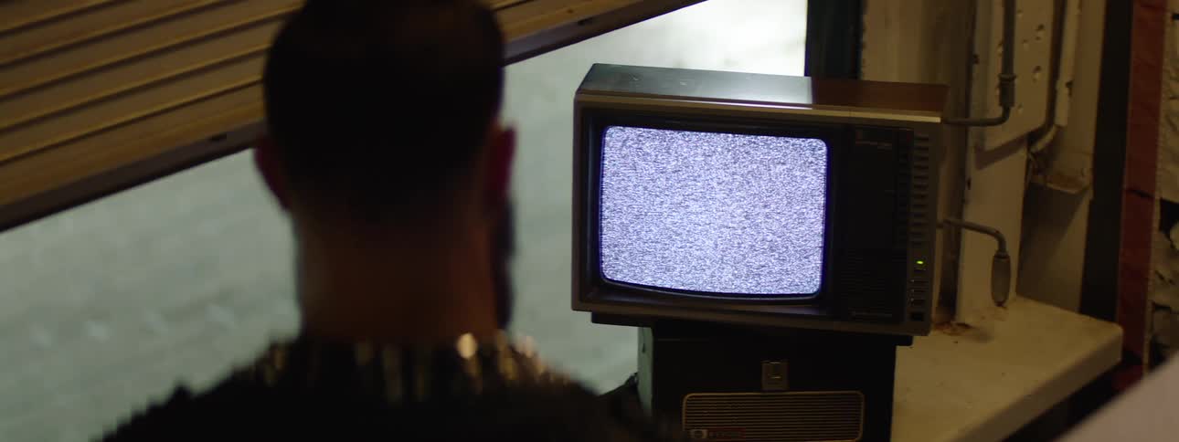 Man watches static on an old television inside a dimly lit room