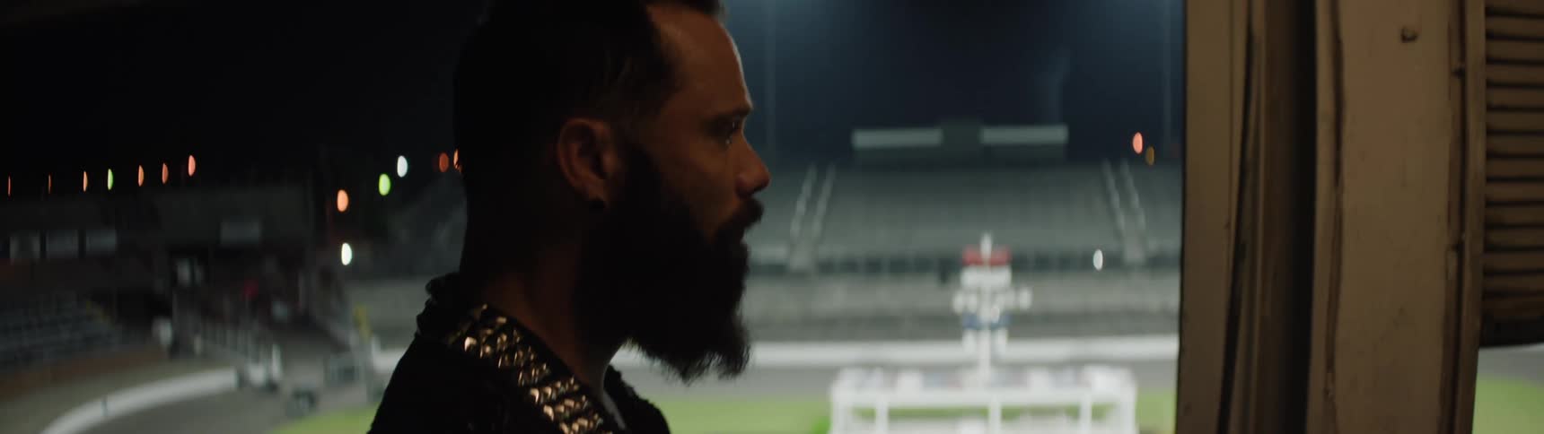 Man observing empty stands of a stadium lit up at night