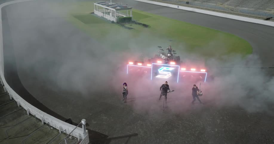 Band performing at a racetrack at night with lights and smoke on stage