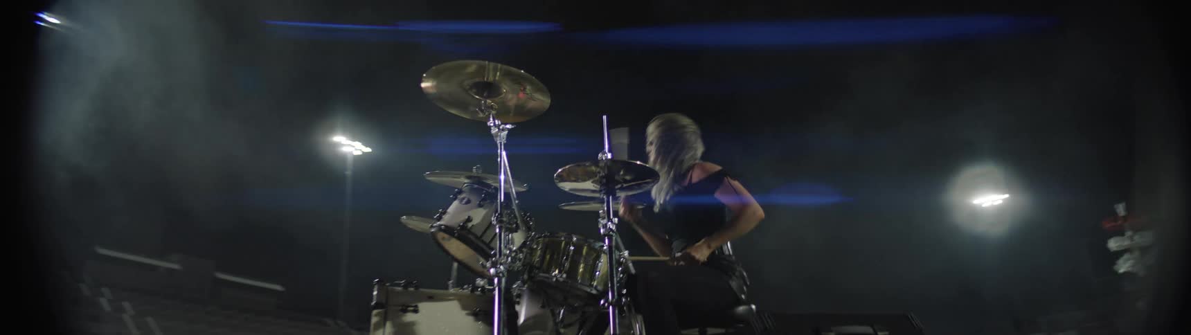 A young blonde female drummer playing a drum set as part of a music band performing at a night concert