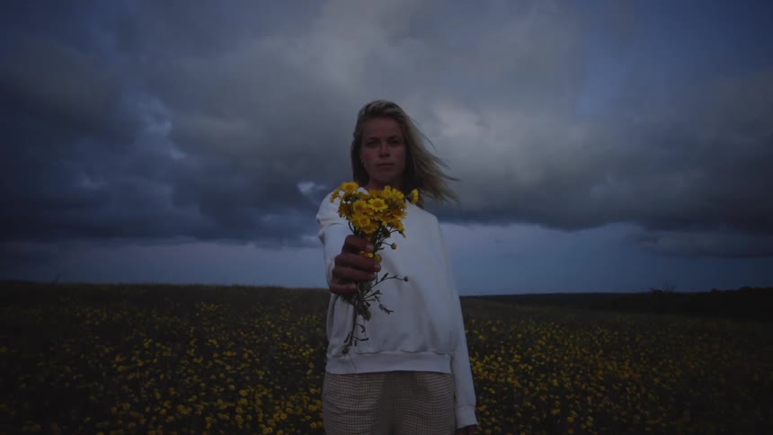 Female holding out daises on a field in the country with storm clouds in the distance