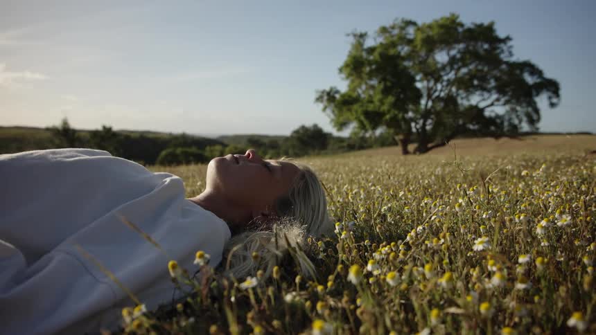 A woman with blonde hair lies on the grassland floor on a sunny day