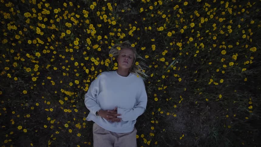 Woman lying in a field covered with small yellow flowers