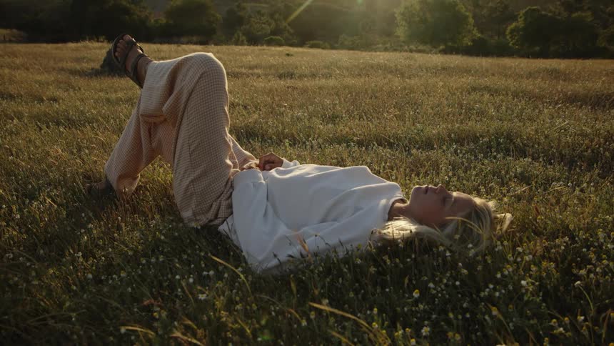 Woman lying on the grass under the evening light in a peaceful field