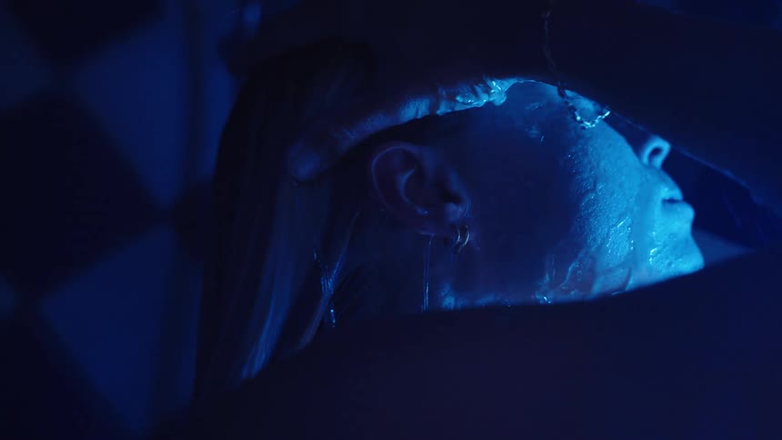 Woman washing her face under intense blue light in a dark setting