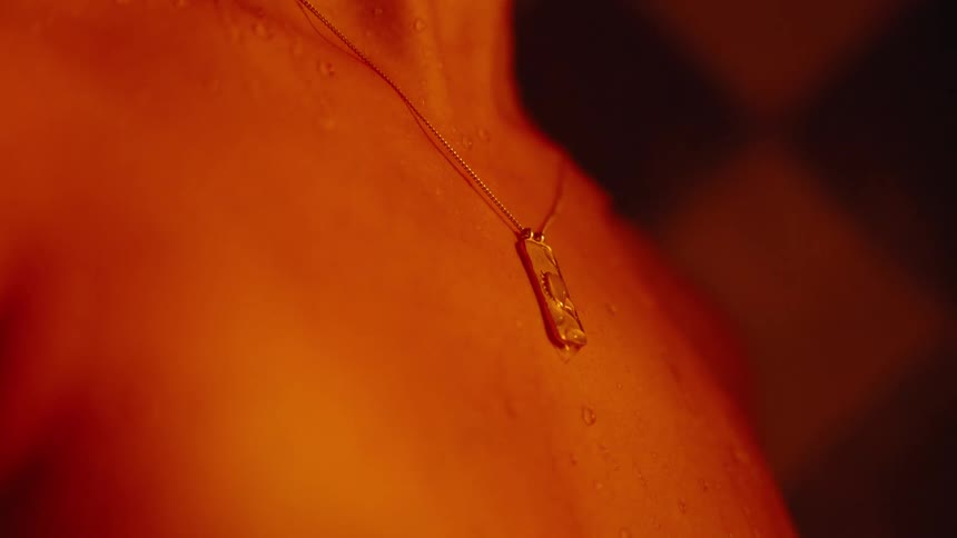 Silver necklace resting on wet skin under orange light