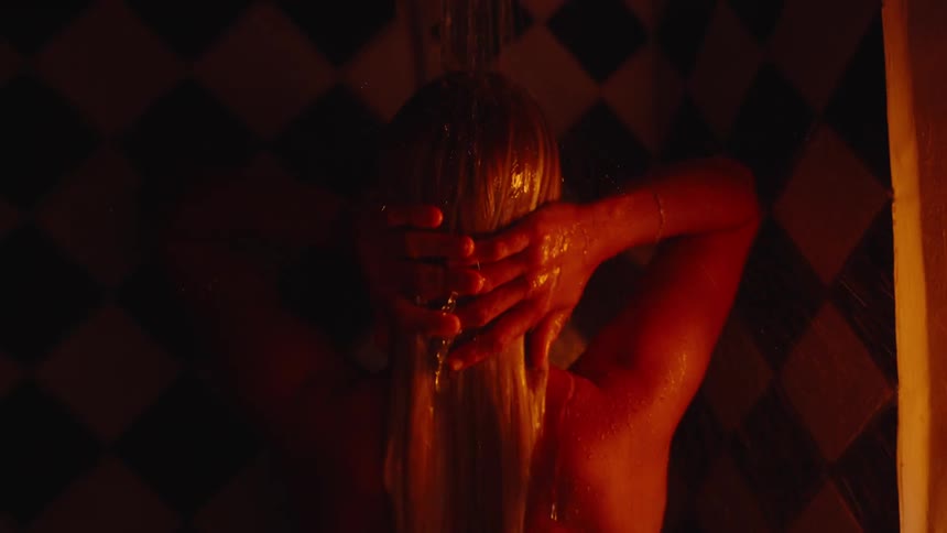 A woman showers under warm light with her hands in her hair