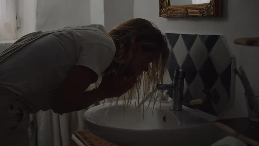 Woman leaning over the sink washing her face in a bathroom lit by natural light