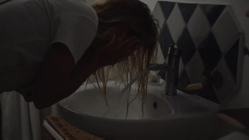 Woman washing her face in a softly lit bathroom sink