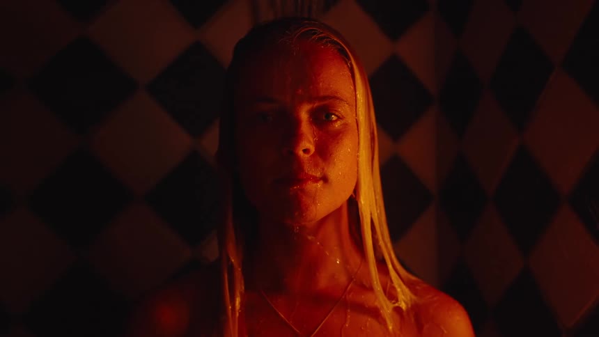 Blonde woman standing in shower in the dark as water drips down her face