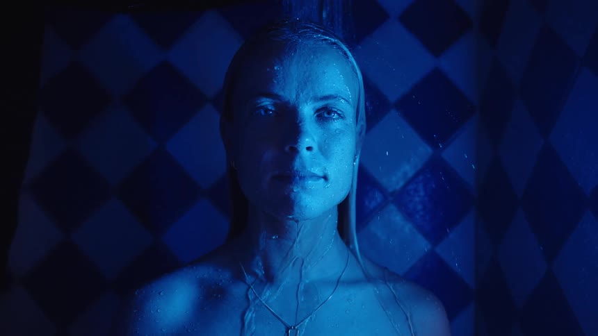 Woman under running water in a space with blue tiles in geometric pattern