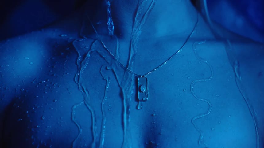 Water running down the body illuminated by intense blue light