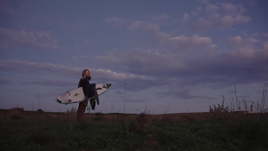 Surfer walking with a board under the evening sky