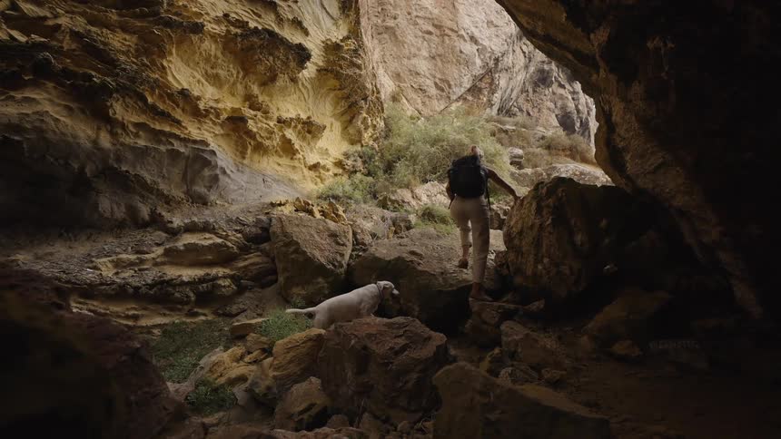 Woman hikes through rocky cave with her dog