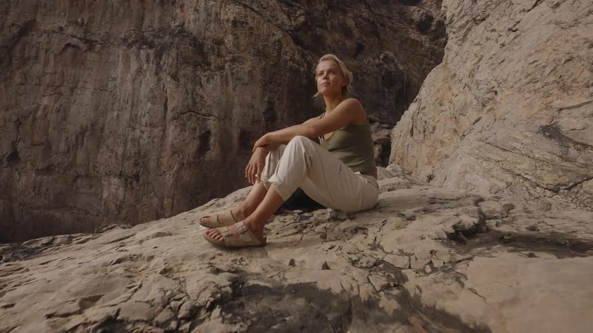 A young blonde woman sitting on top of a rocky mountain