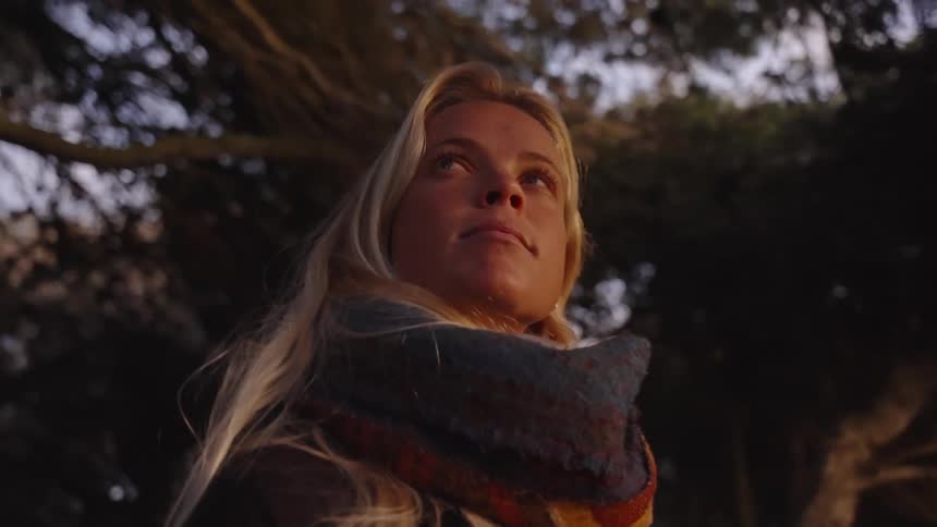 A young blonde woman under a tree looking up and around