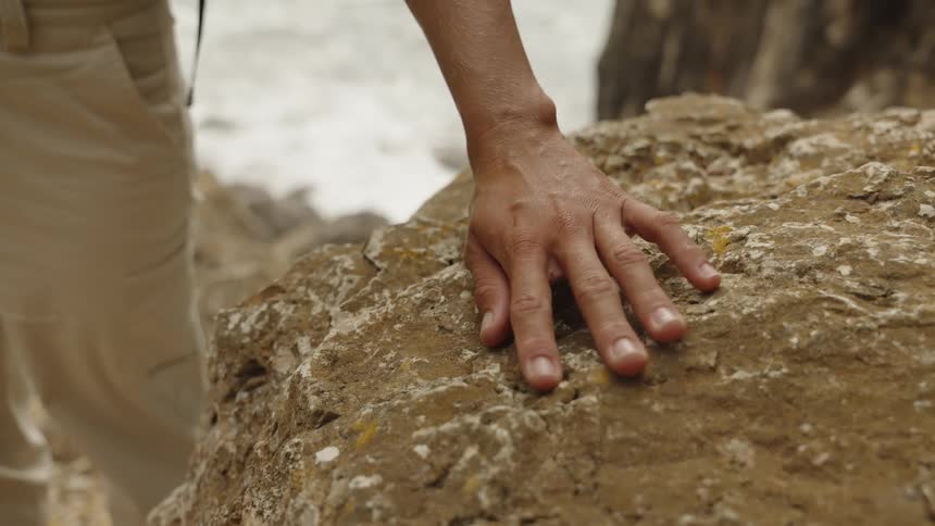 Hand rests on roughtextured rock in a natural setting with earthy tones and uneven surface