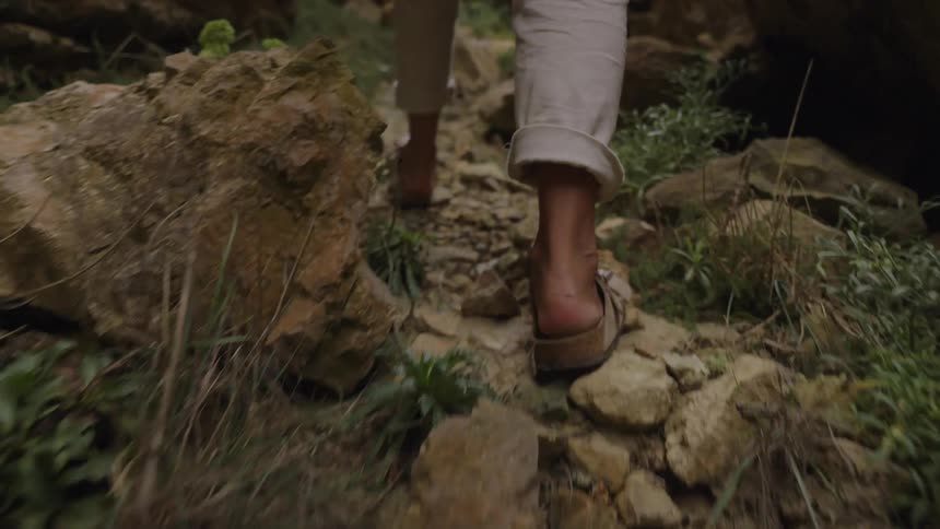 Person walking along a narrow trail surrounded by rocks and low vegetation