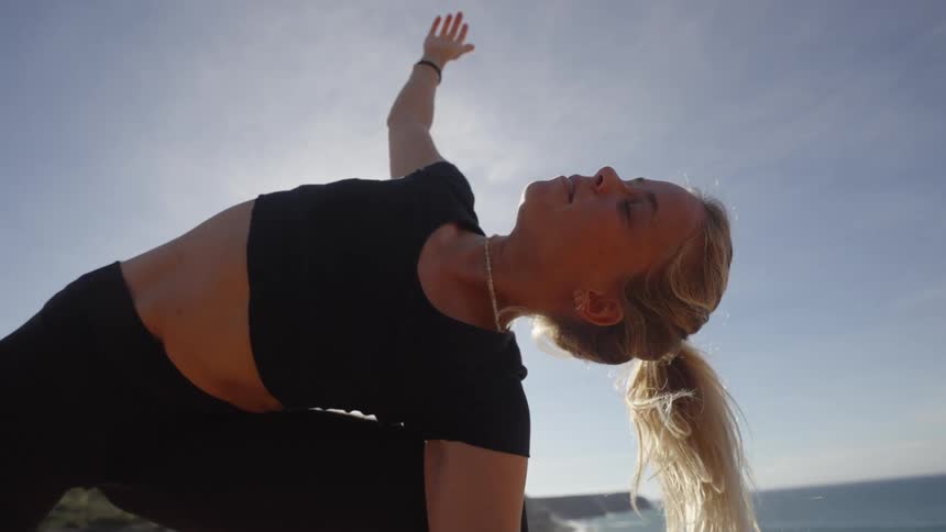 Woman practicing yoga outdoors with her arm extended under the sun