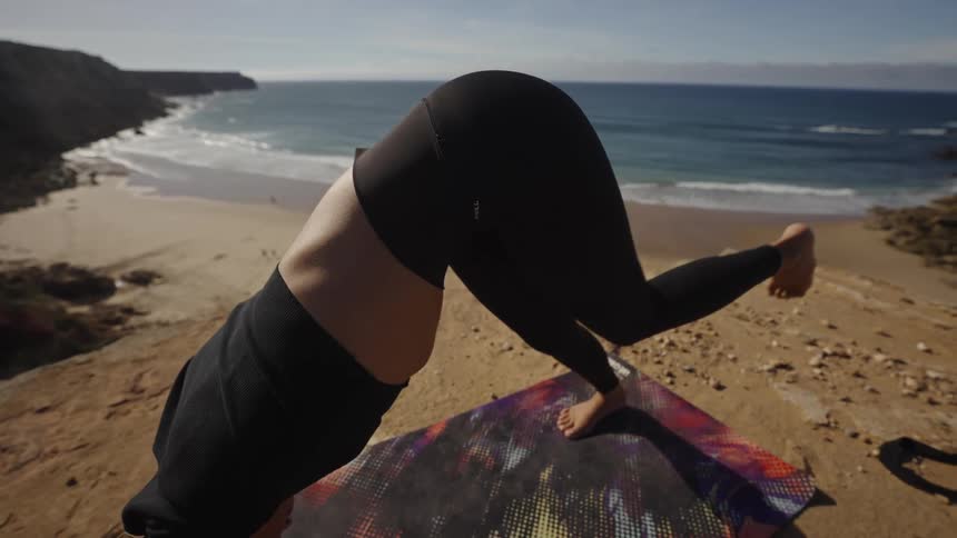 A woman stretching on a mat on the sand at the beach