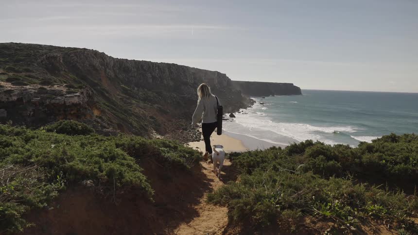 Woman walking along a coastal trail with a dog overlooking the sea