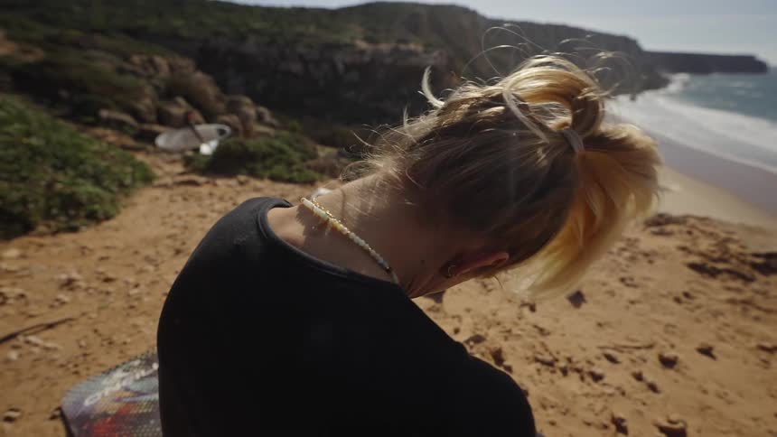 Woman with tiedback hair leans on rocky ground while stretching near resting dogs
