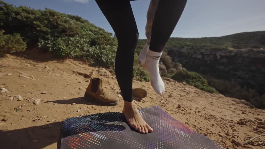 Woman taking off her socks on a board in a sandy area with vegetation