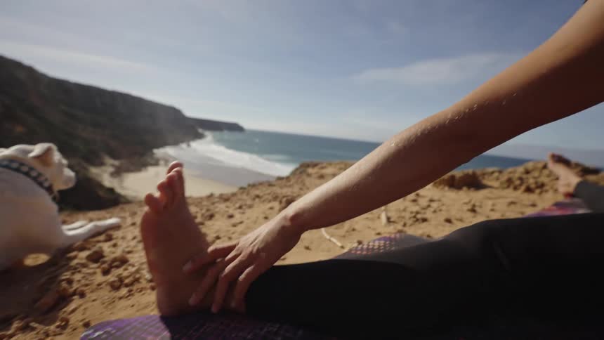 A young woman stretching near the sea with a dog lying beside her