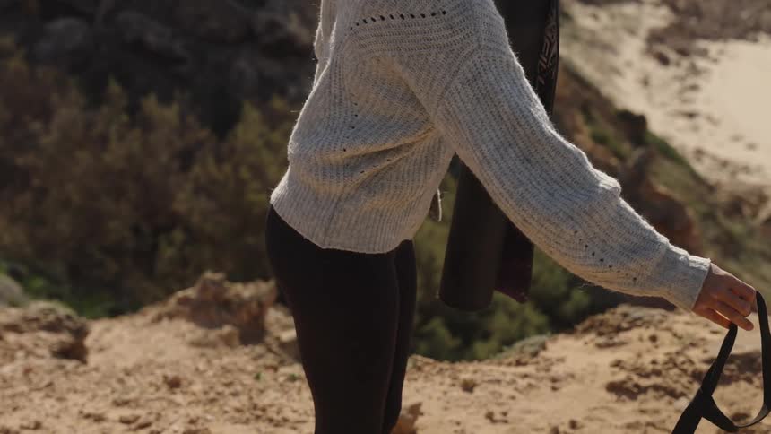 Woman unrolls a yoga mat onto the ground in the mountains while her dog stands nearby
