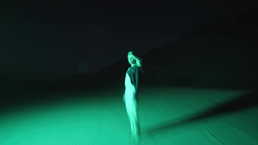 Woman standing under intense green light in a dark deserted area