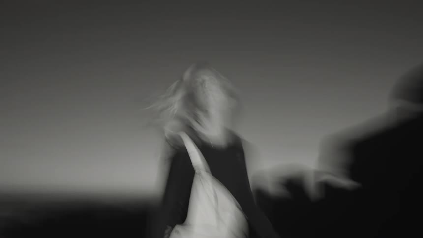 A person wearing light pants and a dark top is shown moving quickly on a flat surface the persons figure is blurred from the speed of the motion and the background is a uniform dark gray