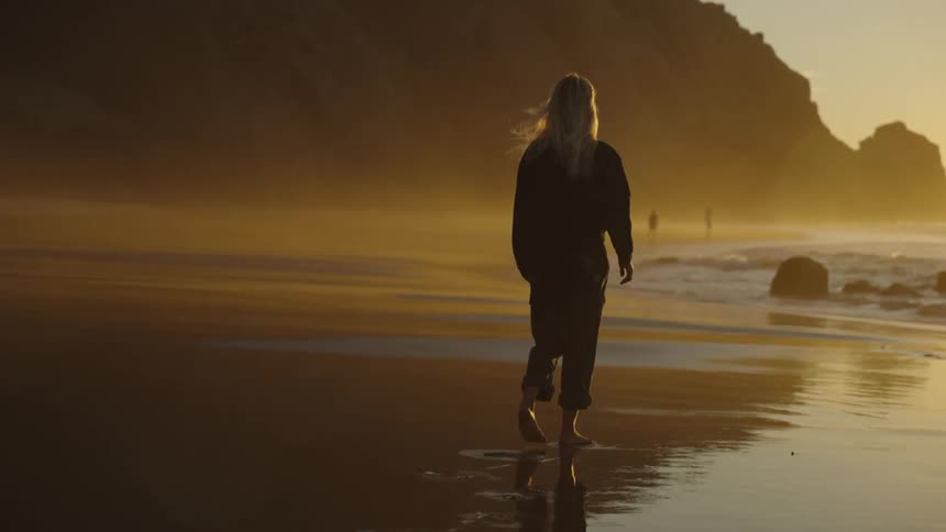 A woman walking on the beach at sunset