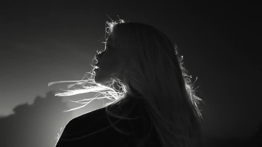 Woman in profile with hair blowing in the wind under bright light in black and white
