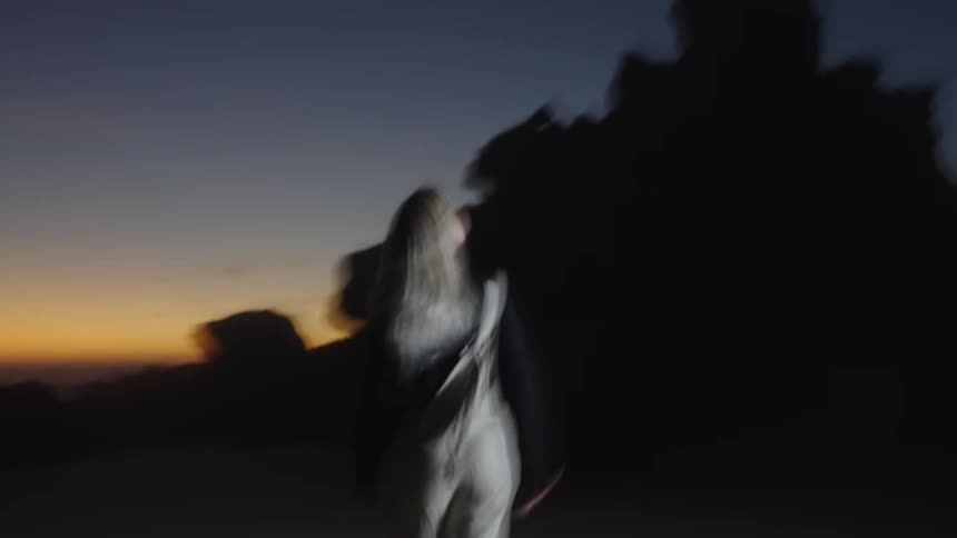 A young woman with blonde hair stands on the beach sand at dawn