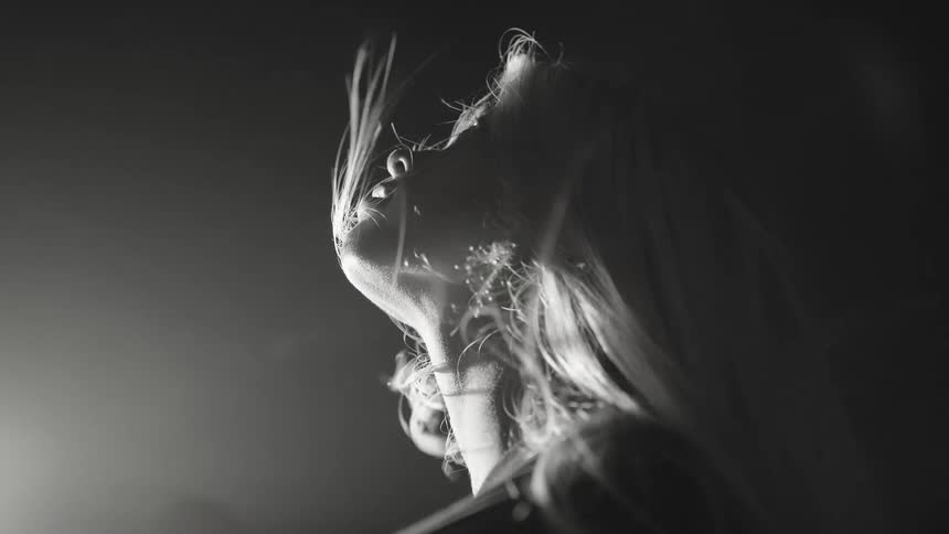 Woman in blackandwhite closeup with face turned toward the light and hair blowing in the wind