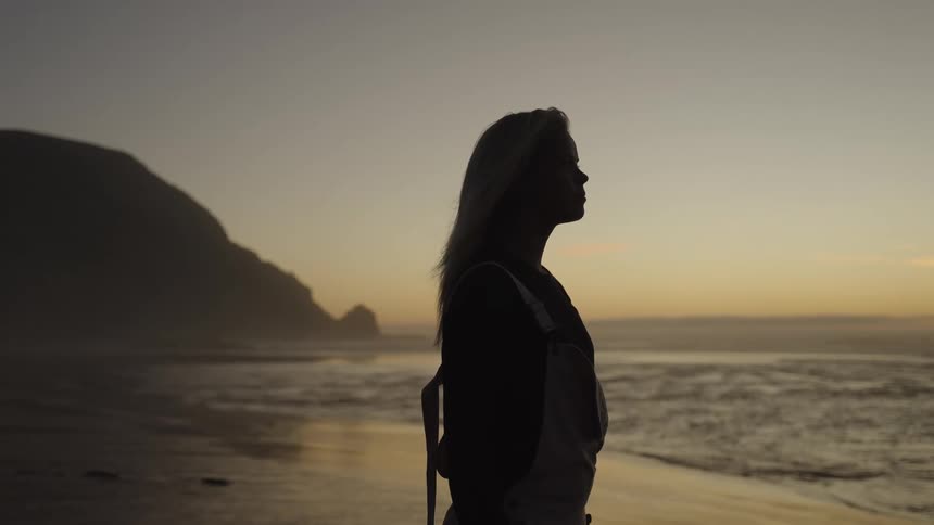 Woman watching the sea at dawn with her silhouette against the horizon
