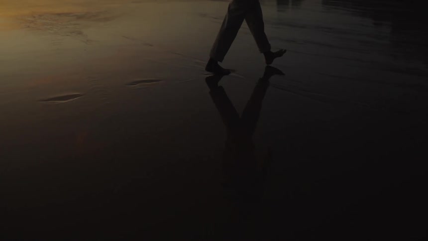 A female walks along a beach leaving a trail of footprints in the wet sand