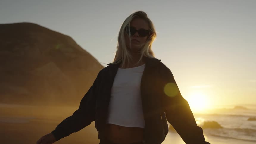 Woman wearing sunglasses walking on the beach at sunset